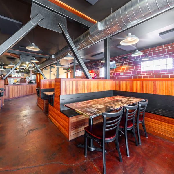 Restaurant interior with wooden booths, exposed brick, industrial ceiling, and a long counter in the background.