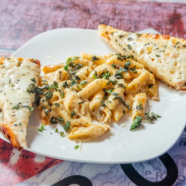Creamy penne pasta with fresh basil and two slices of cheesy garlic bread on a white plate.