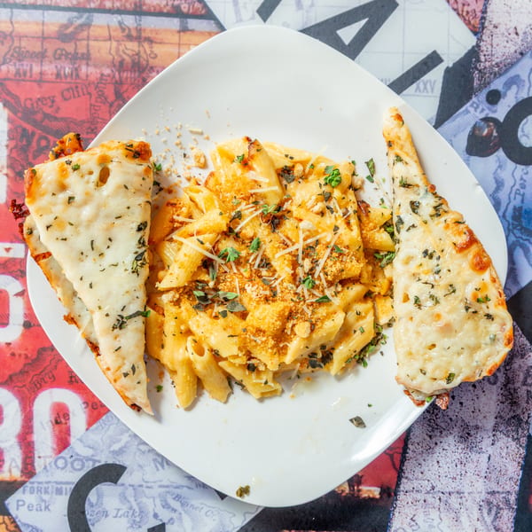 Creamy penne pasta with breadcrumbs and herbs, served with two cheesy garlic bread slices.