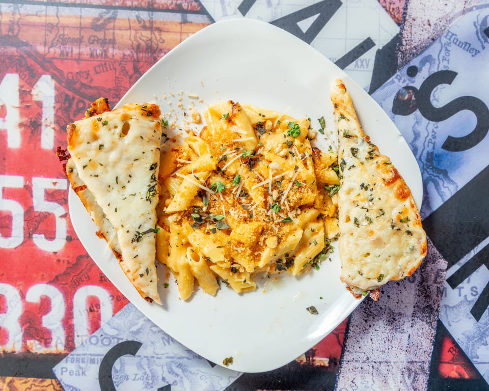 Creamy penne pasta with breadcrumbs and herbs, served with two cheesy garlic bread slices.