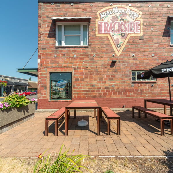 Trackside Pizza's brick exterior with outdoor seating, a Pepsi umbrella, and a large pizza mural.