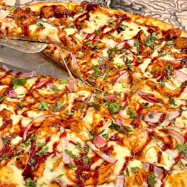 A slice of BBQ chicken pizza with red onions and cilantro is lifted from a whole pizza.